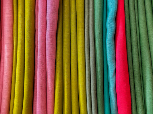 Colorful folded fabric swatches representing lawn, cambric, and cotton textiles